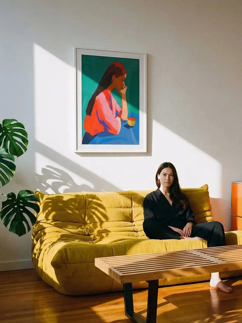 Modern living room with yellow sofa, woman seated, colorful art print on wall, sunlight streaming in