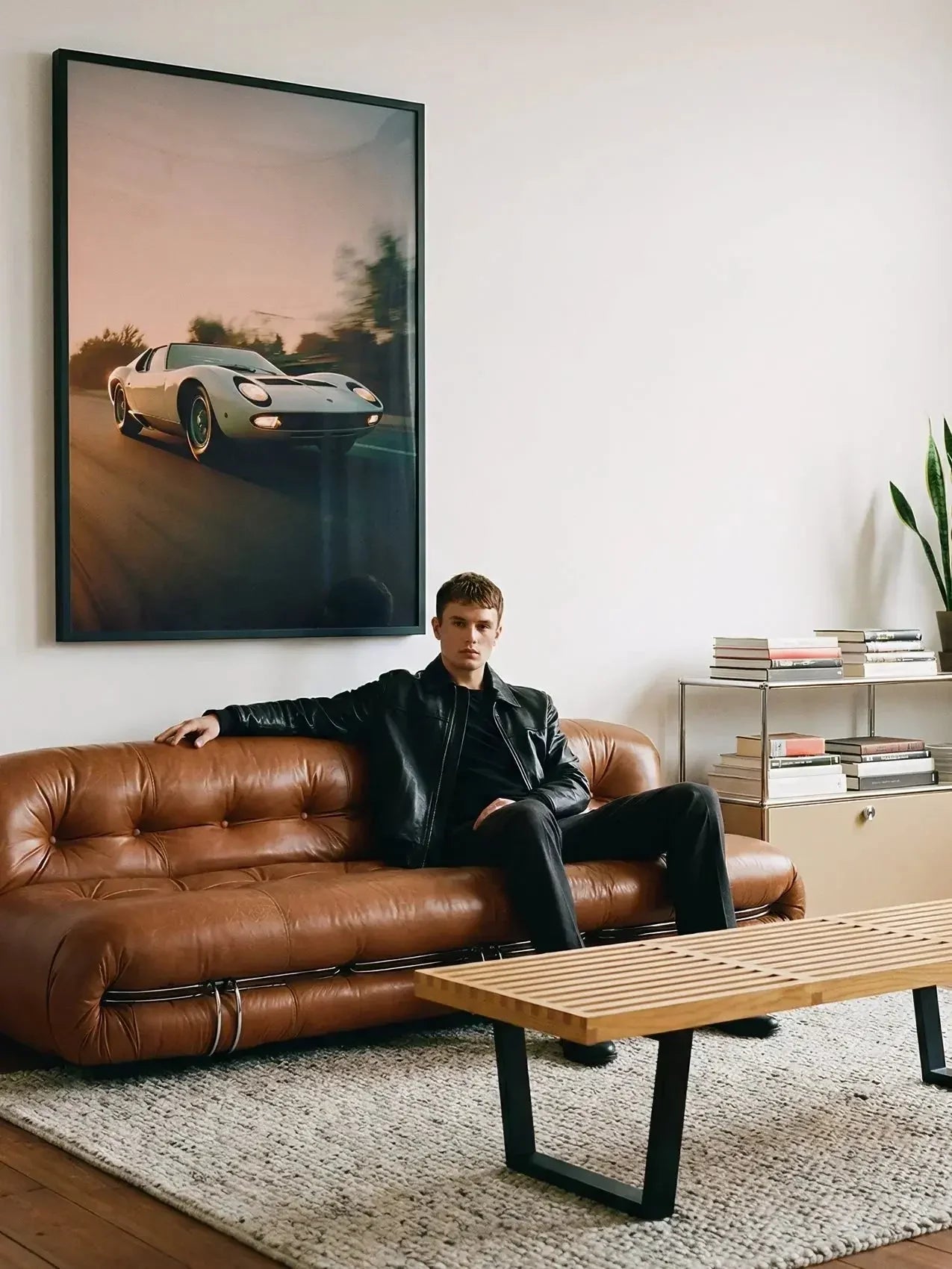 Modern living room with a brown leather sofa, a man seated, and a Lamborghini Miura poster on the wall