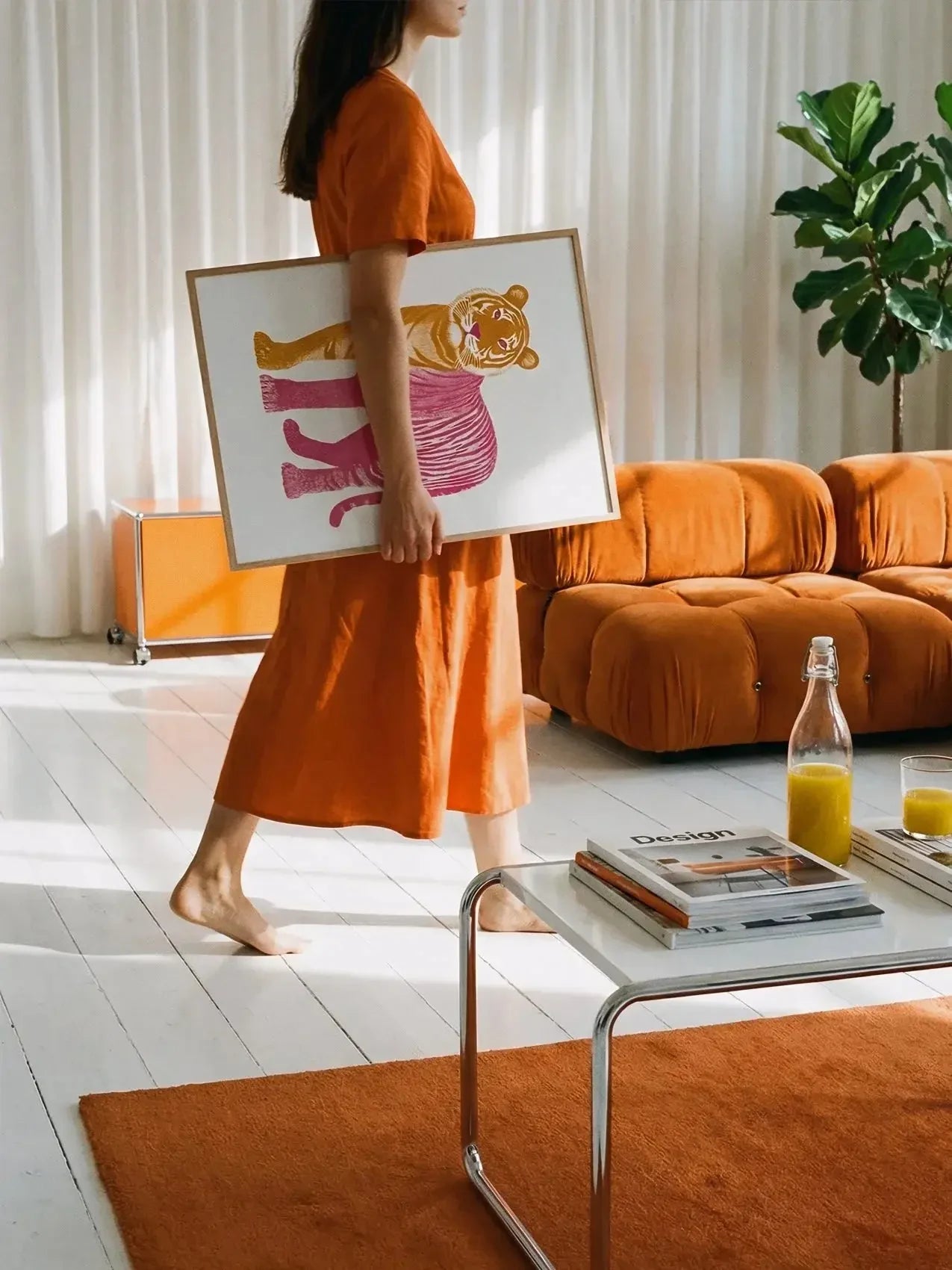 Woman holding colorful tiger art print in modern orange-themed living room